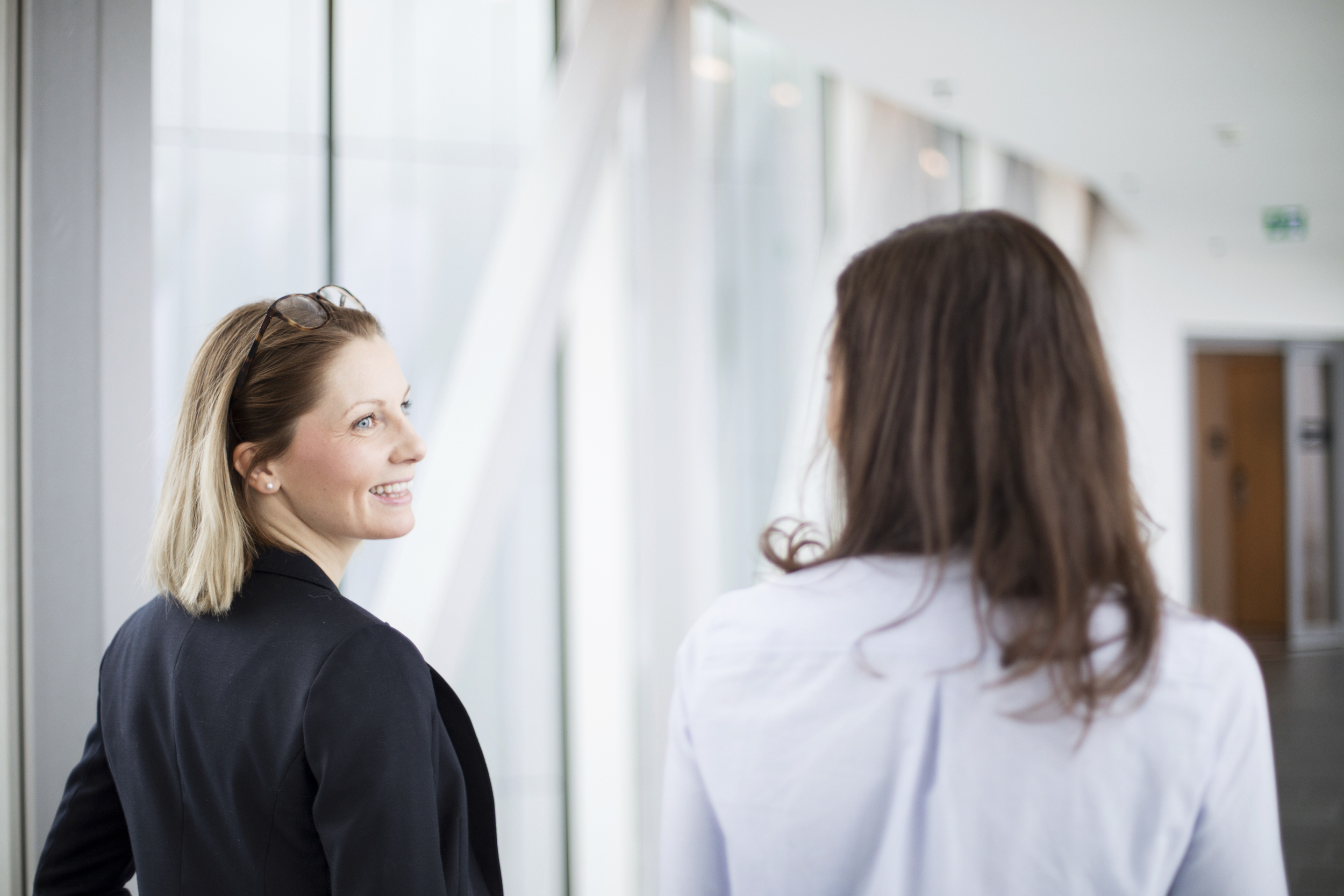 Kvinnelige kollegaer ser på hverandre og smiler i en gang