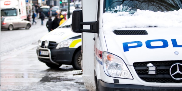 Politibil parkert i snødekt gate med andre biler og folk i bakgrunnen i en by
