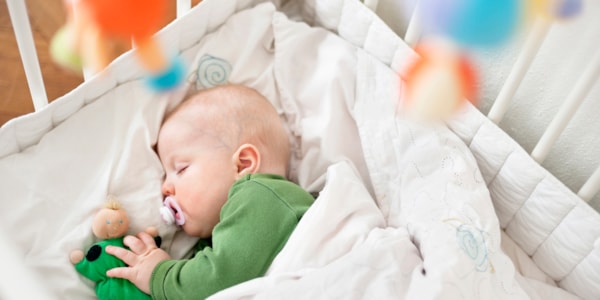 Baby som sover i sprinkelseng med smokk i munnen