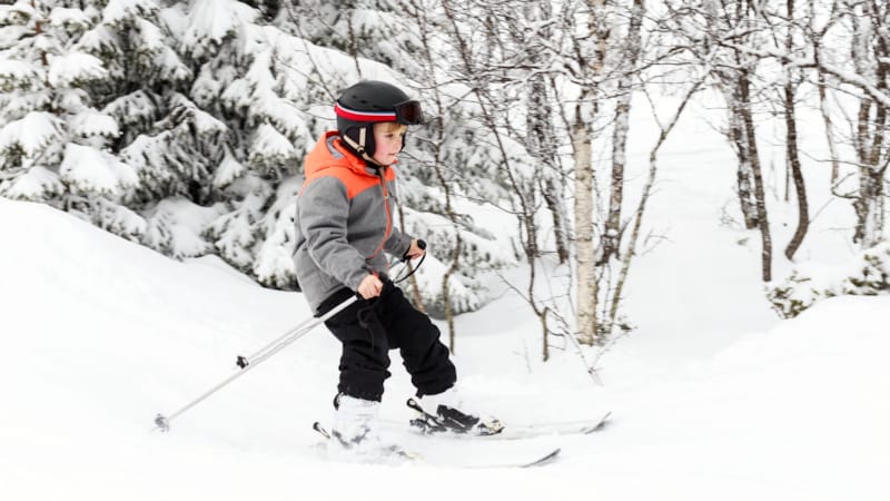 Gutt på ski med hjelm i skogsløype