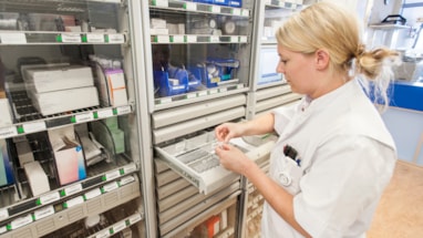 Farmasøyt foran hyller med medisiner i et apotek