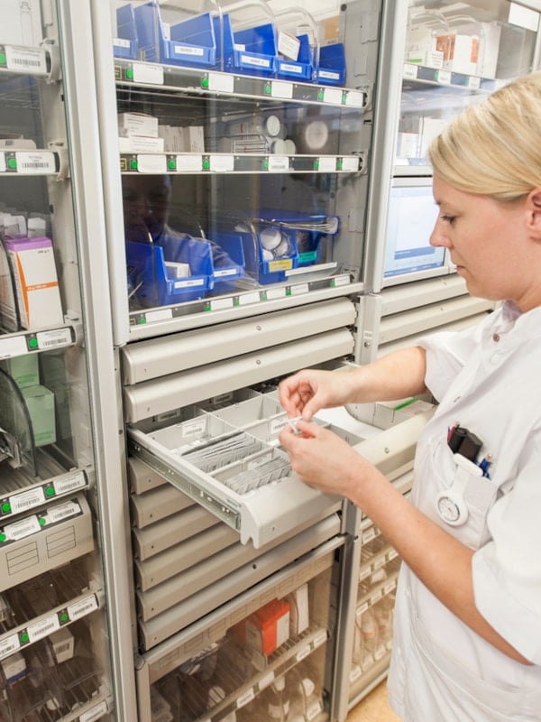 Farmasøyt foran hyller med medisiner i et apotek