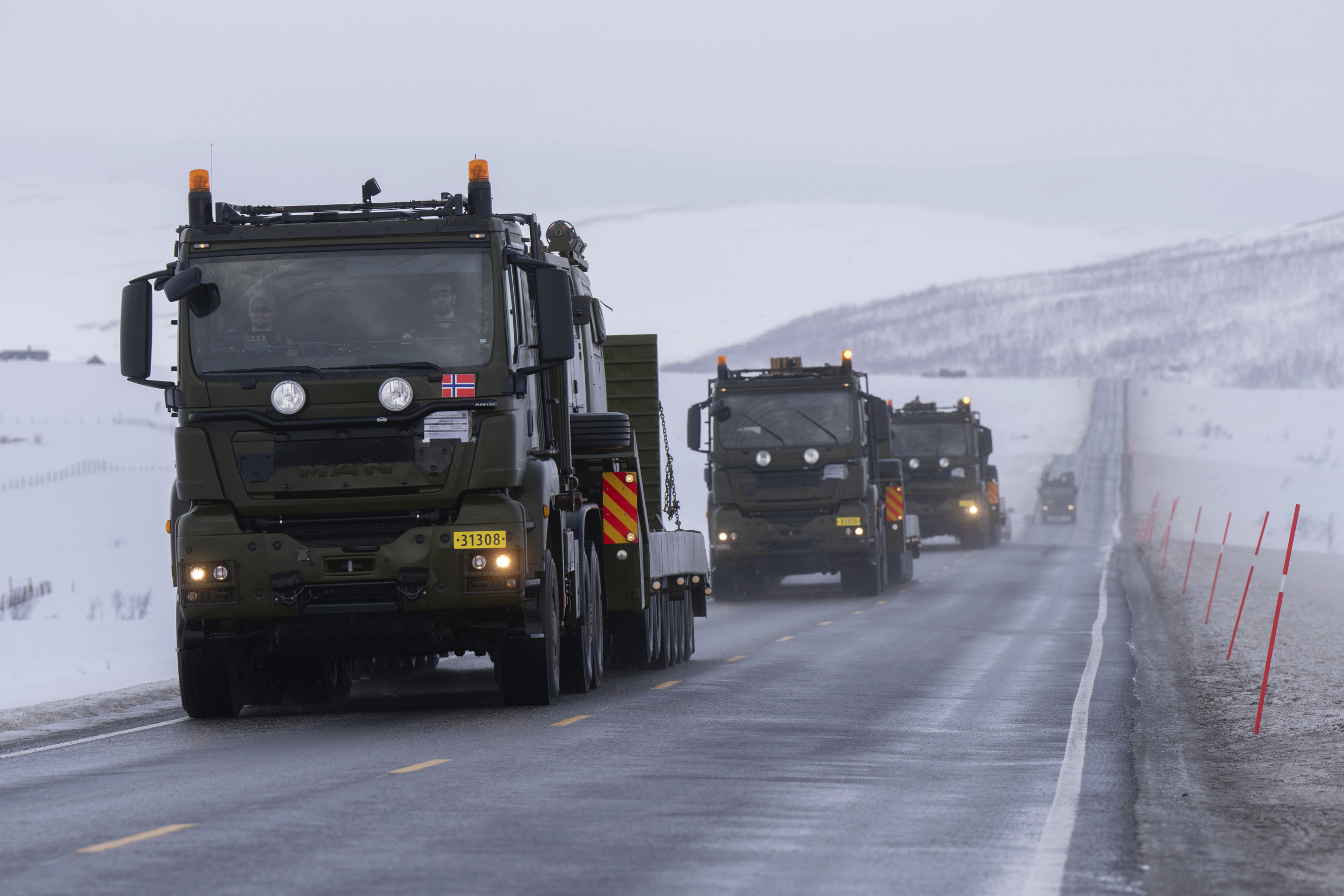 Grønne lastebiler med norsk flagg kjører i vinterlandskap