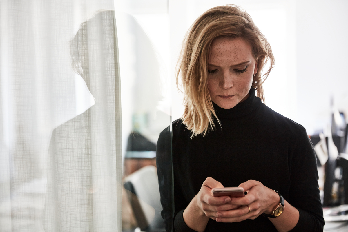 Kvinne som ser alvorlig ned på en mobiltelefon som hun holder med begge hender