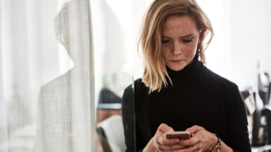 Kvinne som ser alvorlig ned på en mobiltelefon som hun holder med begge hender