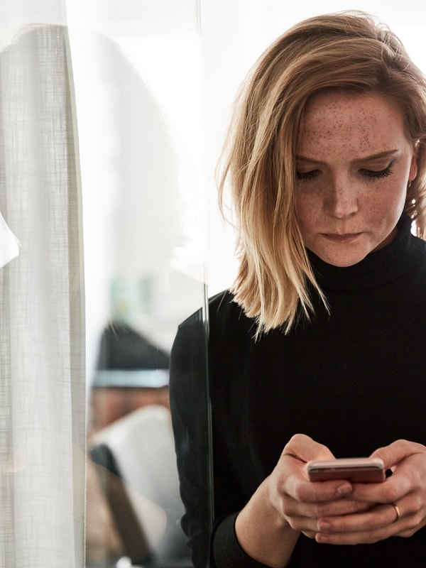 Kvinne som ser alvorlig ned på en mobiltelefon som hun holder med begge hender