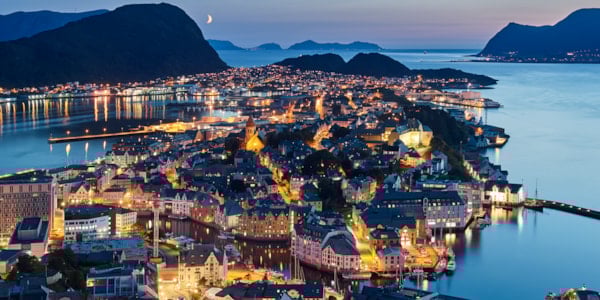 Oversiktsbilde av norsk by ved kysten. Det er halvmørkt og det lyser fra hus og gater.