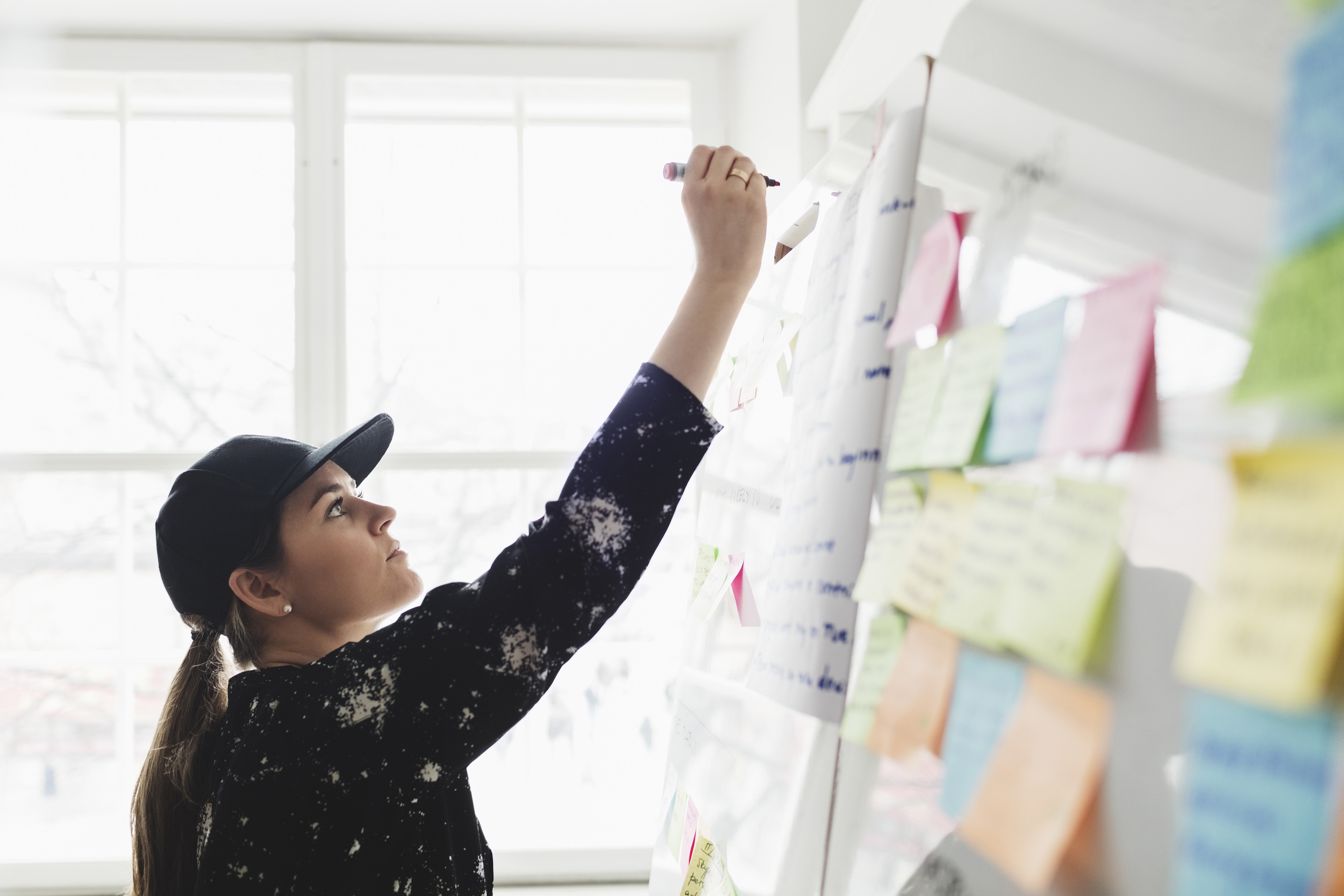 Dame med caps som skriver på lapper på en tavle