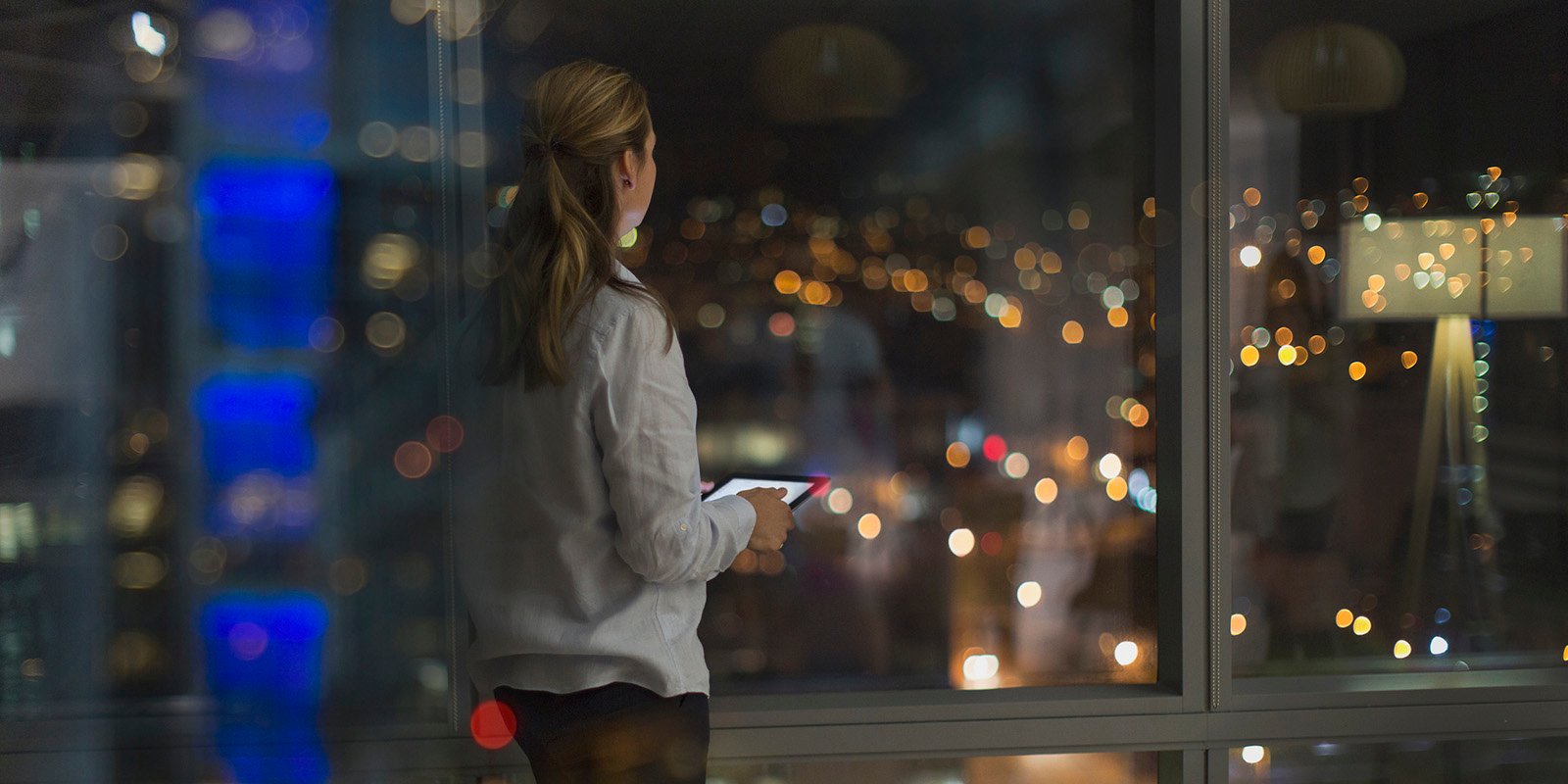 Kvinne som står og kikker ut av et kontorlokale med digitale lys