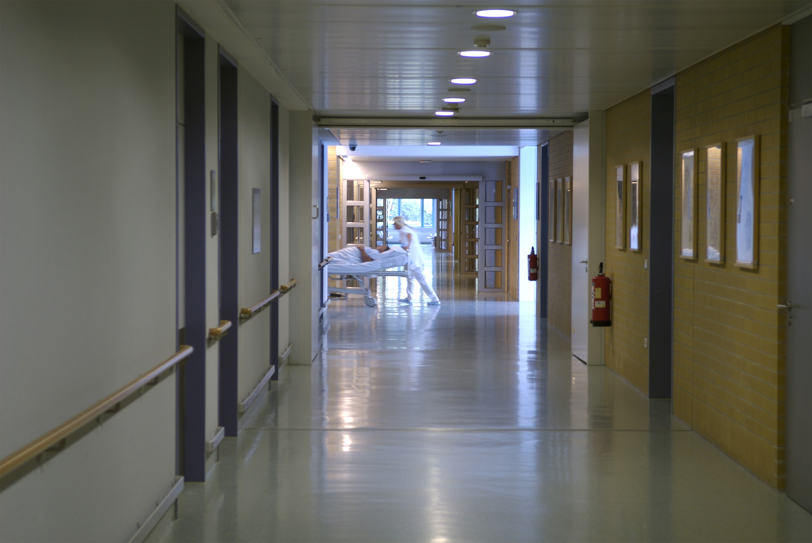 Svakt belyst sykehusgang der man skimter helsepersonell som triller en pasientseng