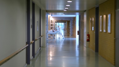 Svakt belyst sykehusgang der man skimter helsepersonell som triller en pasientseng