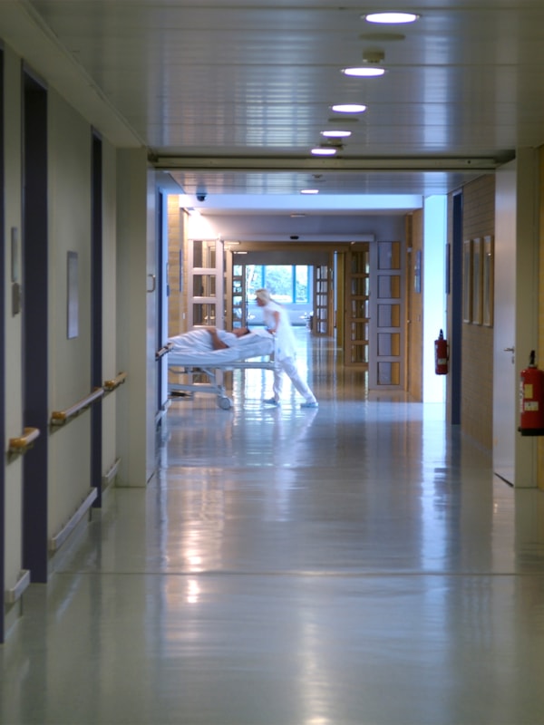 Svakt belyst sykehusgang der man skimter helsepersonell som triller en pasientseng