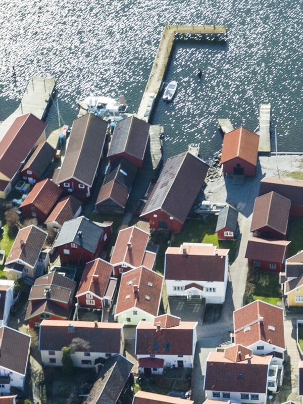 Luftfoto av en norsk kystlandsby med flere hvite og røde hus ved sjøen. Dokkingplasser og småbåter langs bryggen. Naturskjønn utsikt over vannet