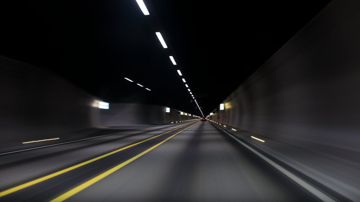 Innsiden av en mørk vegtunnel med lys i taket og gule veimarkeringer