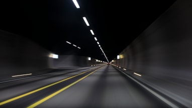 Innsiden av en mørk vegtunnel med lys i taket og gule veimarkeringer