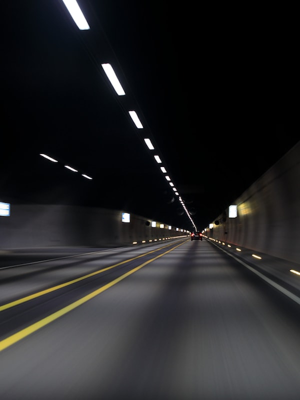 Innsiden av en mørk vegtunnel med lys i taket og gule veimarkeringer