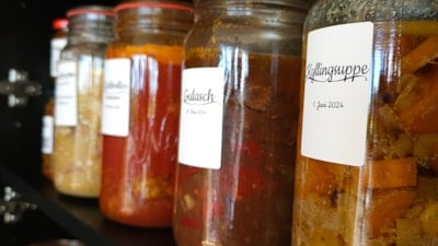 Store og små glas med kvite merkelappar og forskjelleg innhald ståande på svarte lagerhyller.