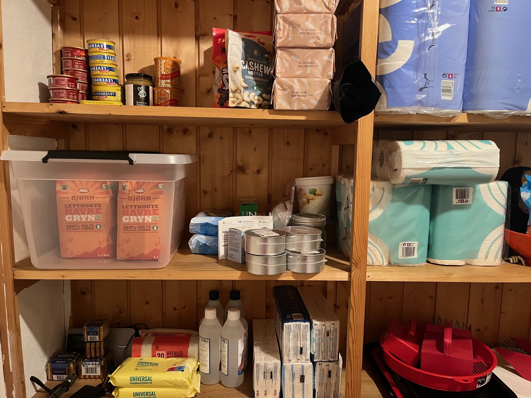 Toalettpapir og ulike beredskapsartiklar ståande på trehylle i ein bod.