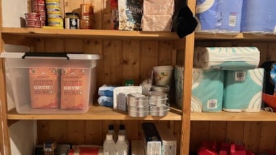 Toalettpapir og ulike beredskapsartiklar ståande på trehylle i ein bod.