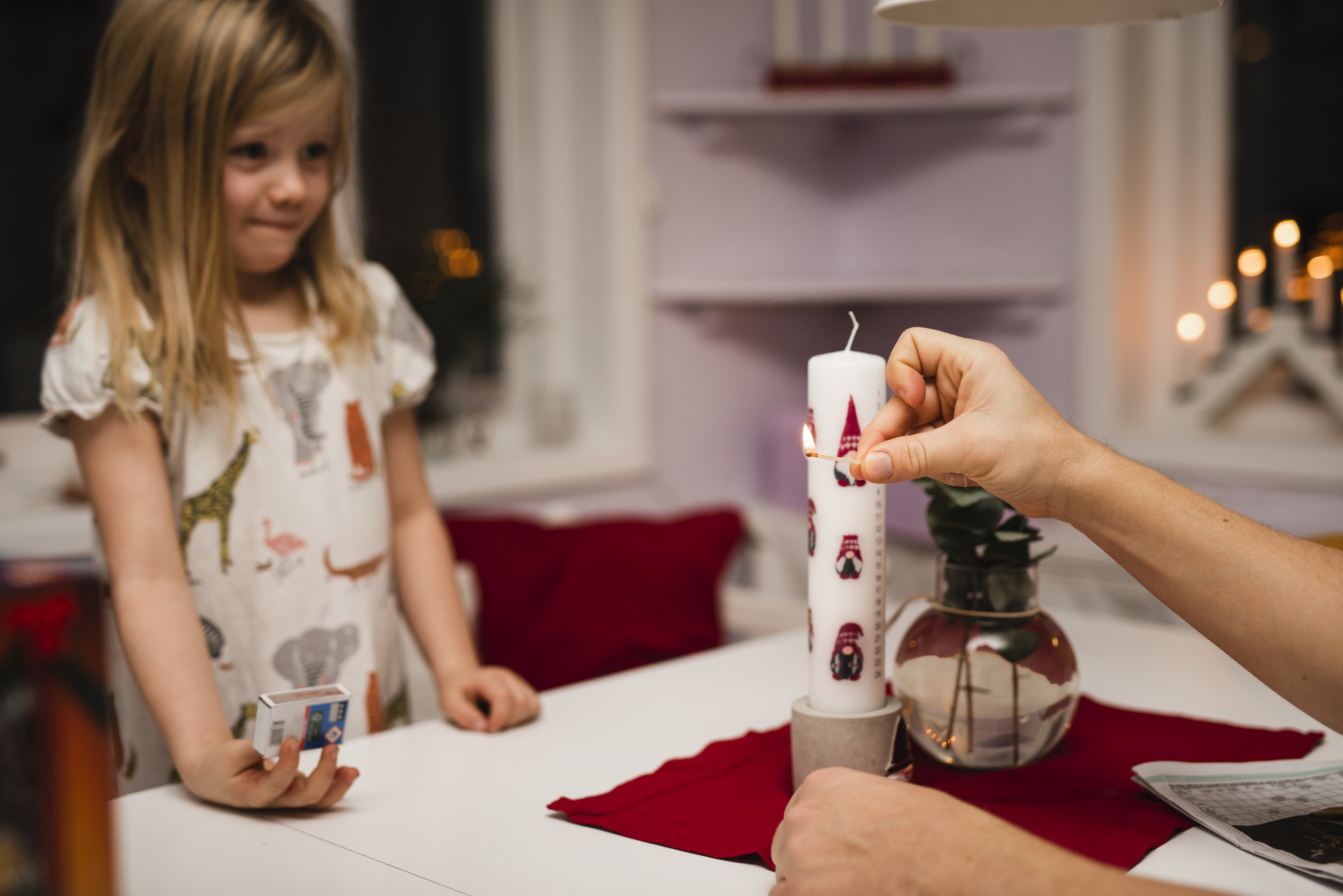 Liten jente som ser spent på en voksen hånd som tenner et julelys