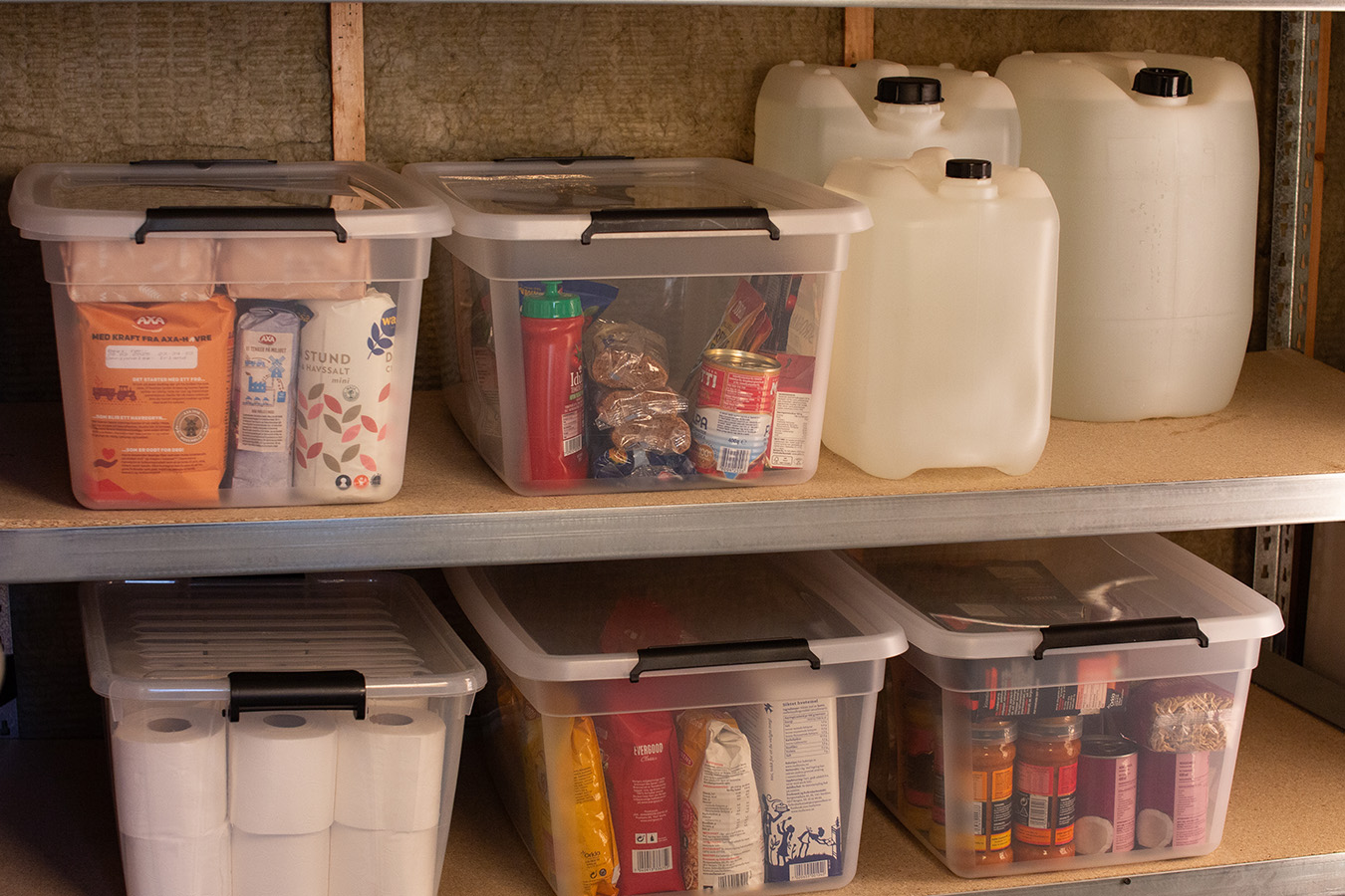 Hyller med vasskanner og plastkasser fylde med tørrvarar, hermetikk og toalettruller.