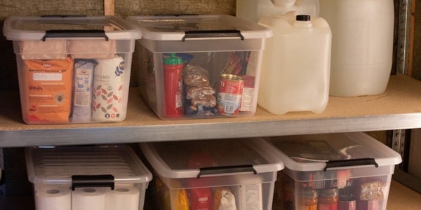 Hyller med vasskanner og plastkasser fylde med tørrvarar, hermetikk og toalettruller.