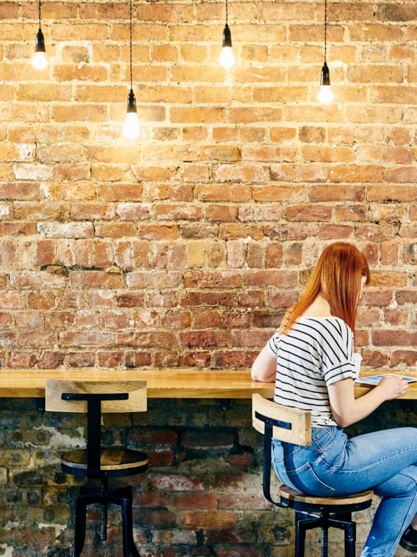 Kvinne som sitter ved en høy benk under en lenke med lyspærer.