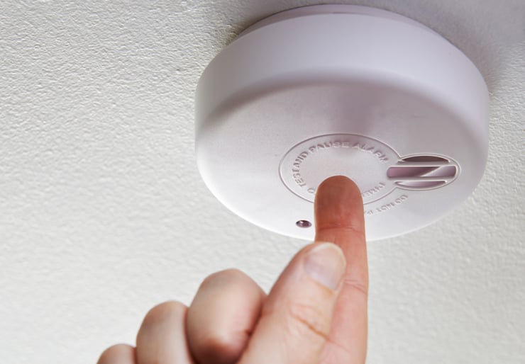 Hånd som trykker på testknappen til en røykvarsler som er montert i taket