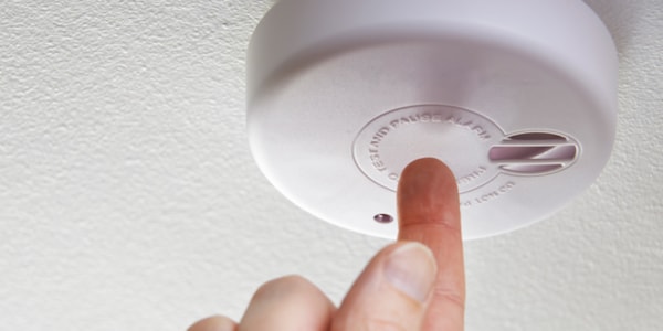 Hånd som trykker på testknappen til en røykvarsler som er montert i taket