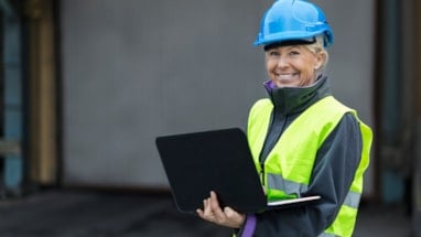 Kvinne med vernehjelm og refleksvest som holder en bærbar pc
