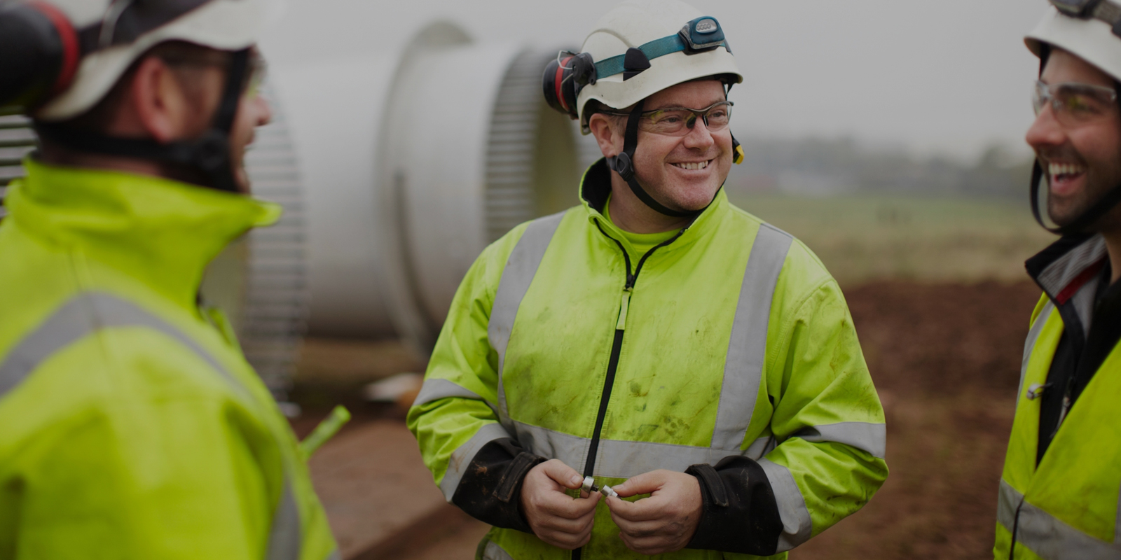 Menn med arbeidsklær og verneutstyr som står og prater på en byggeplass