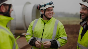 Menn med arbeidsklær og verneutstyr som står og prater på en byggeplass